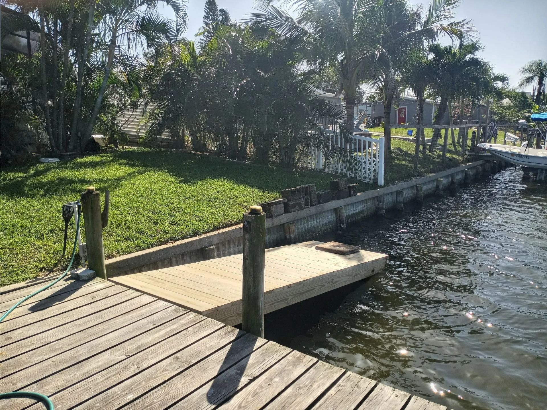 A wooden dock extends into water. A smaller, newer deck is attached. Green grass and trees line the edge.