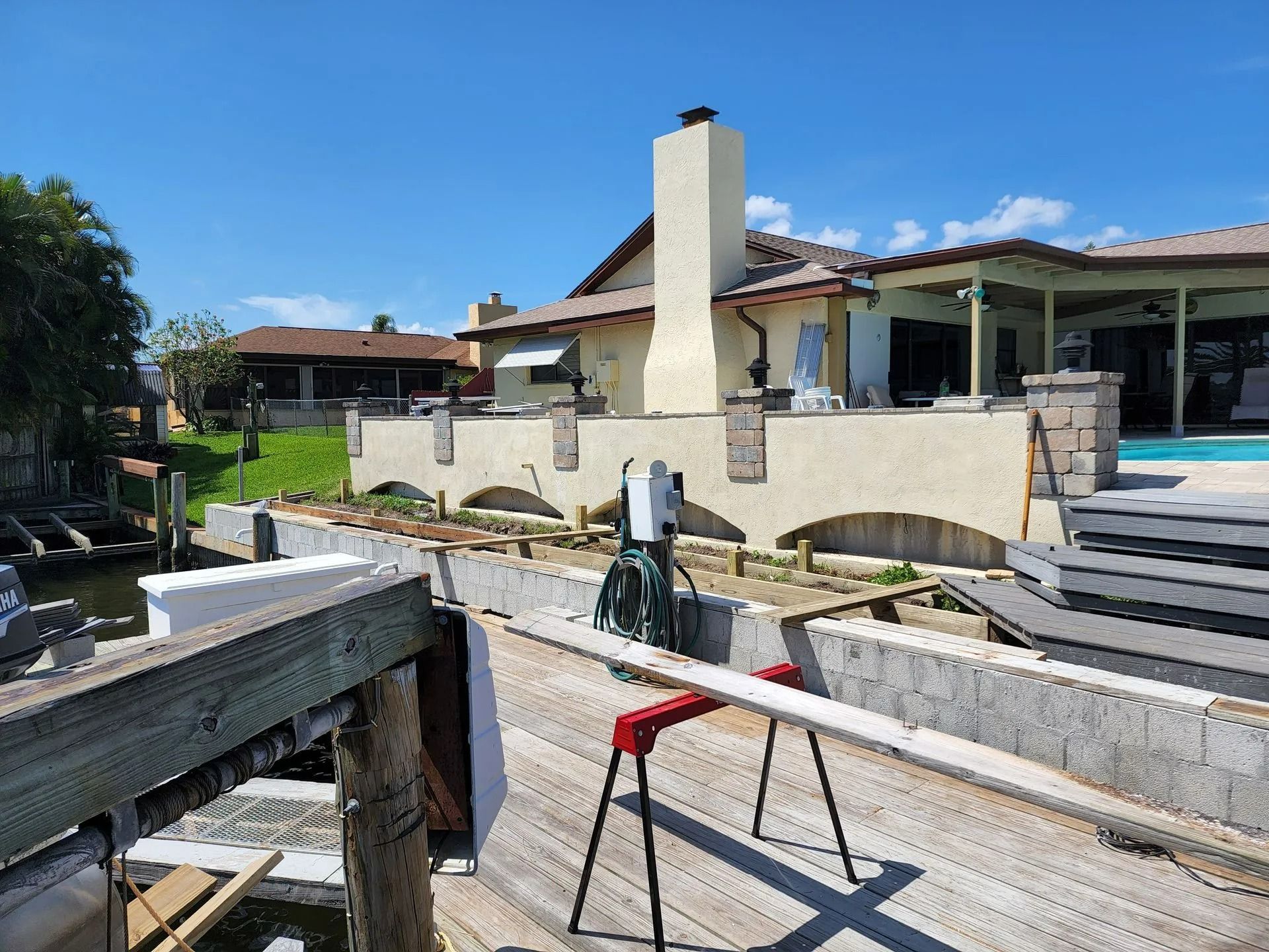 A wooden dock with a laser surveying tool set up in front of a waterfront home under a sunny sky.