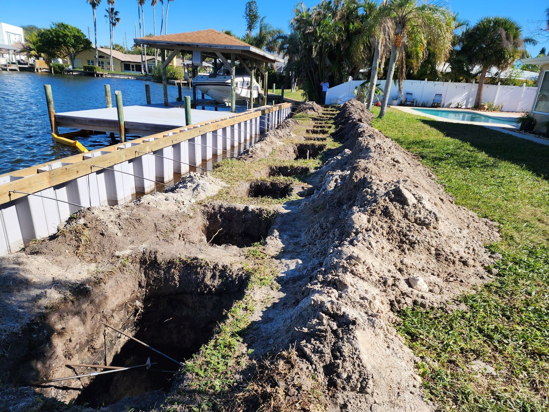 Dock with boat lift over water, wooden deck, surrounding houses and trees under a blue sky.