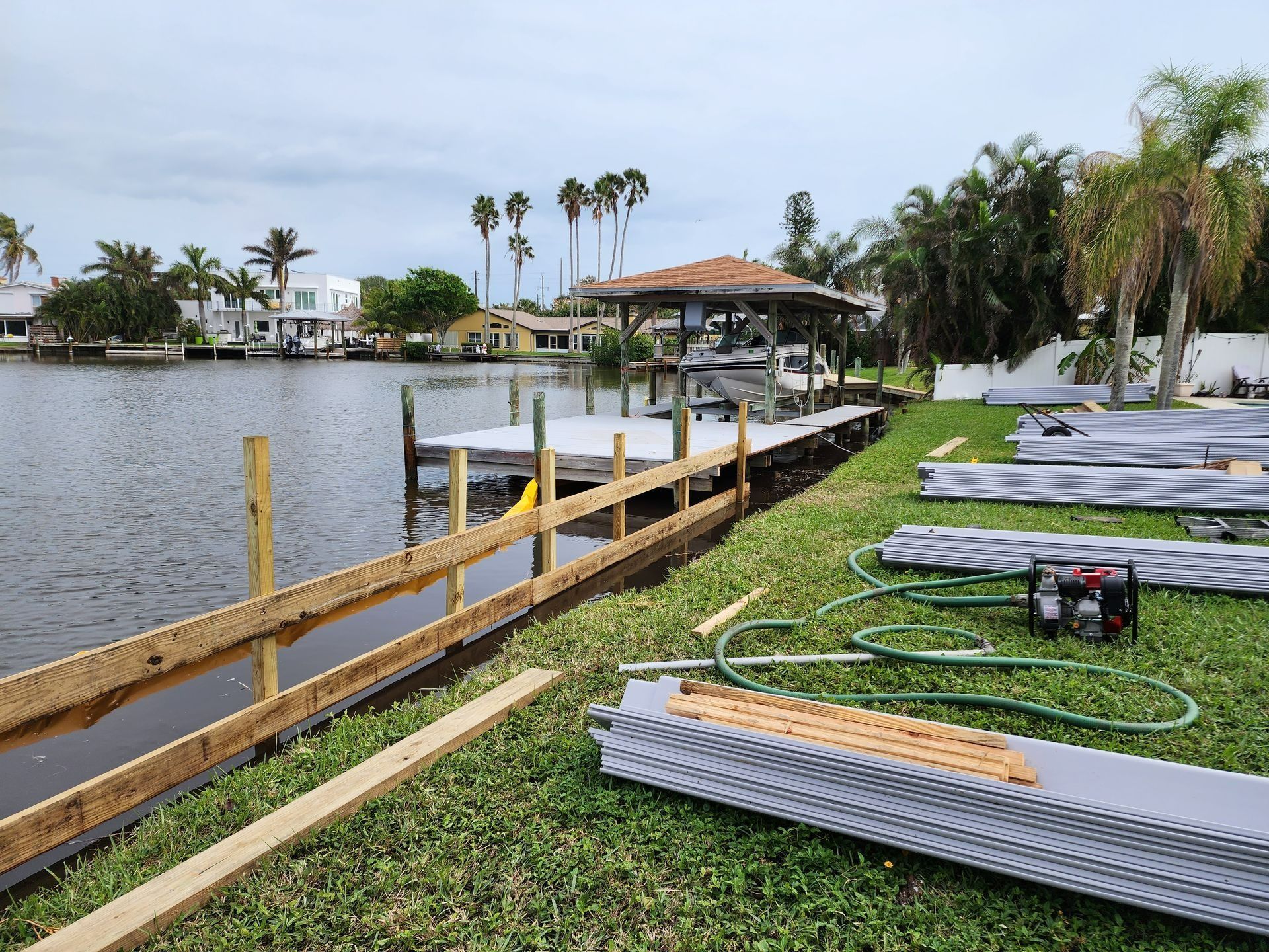Dock with boat lift over water, wooden deck, surrounding houses and trees under a blue sky.