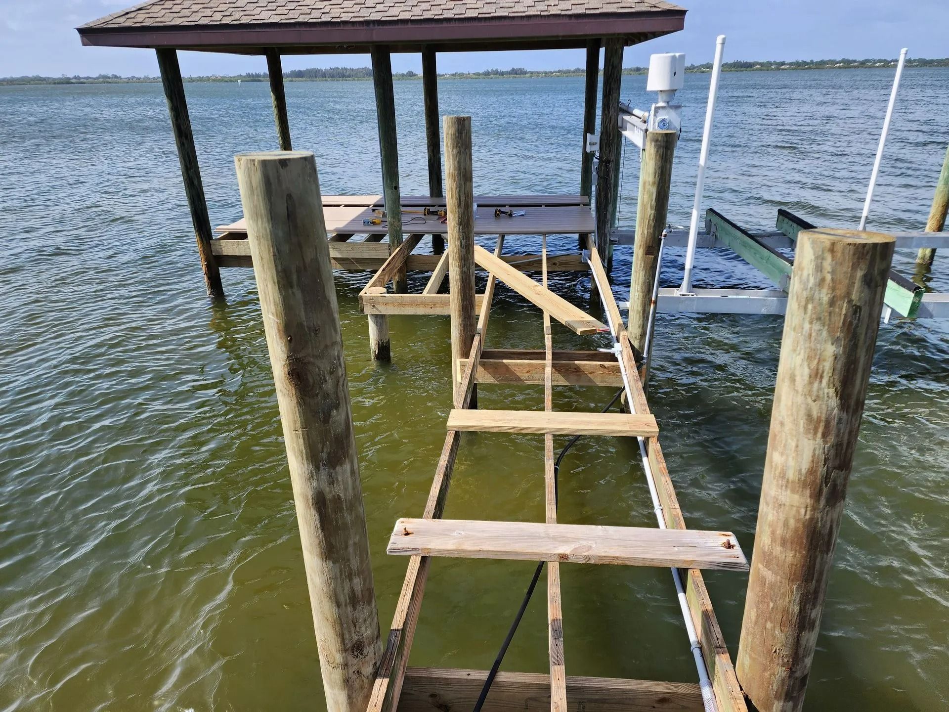 Damaged wooden dock extending into murky water, with a covered sitting area in the background.