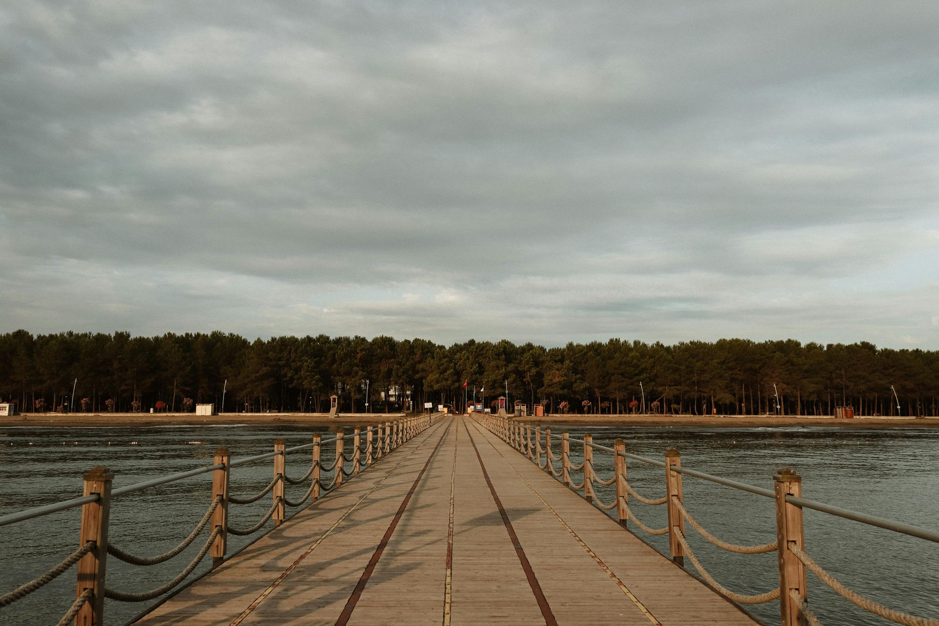 Dock with boat lift over water, wooden deck, surrounding houses and trees under a blue sky.