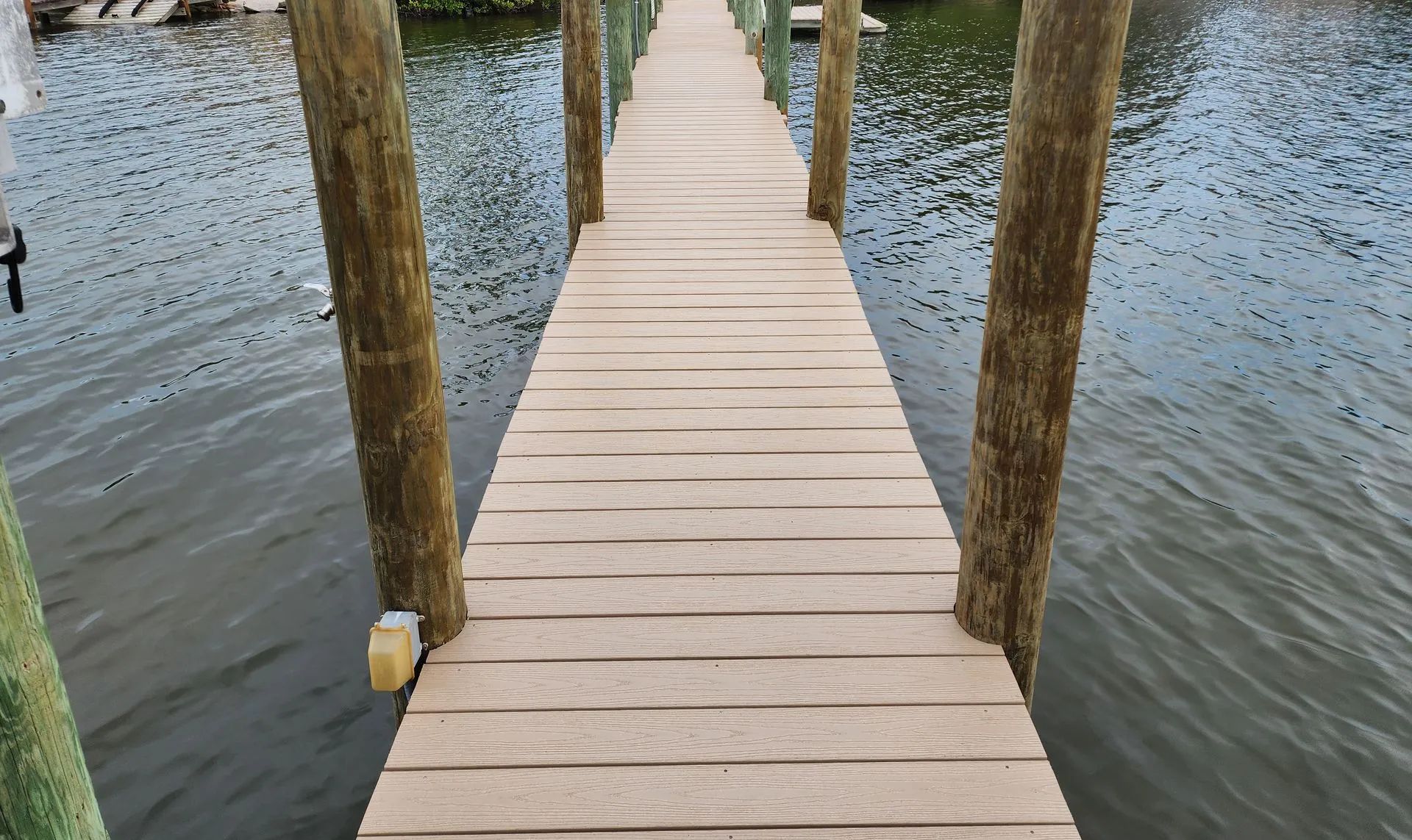 Wooden boardwalk extending over water, flanked by wooden poles, leading toward an unseen destination.