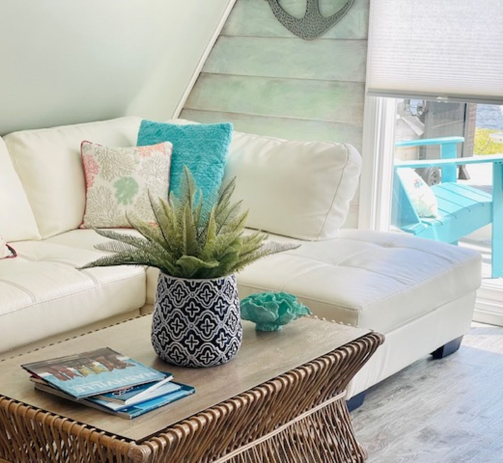 Bright coastal living room with white sectional, turquoise pillows, woven coffee table, and potted plant