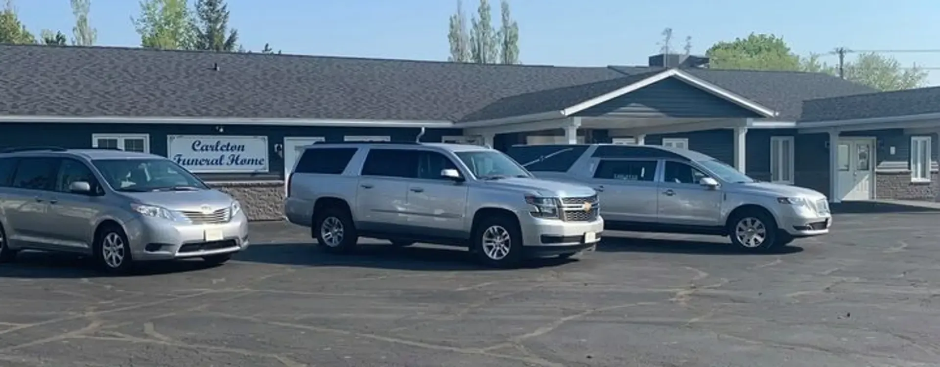 Three silver vehicles parked in front of Carlson Funeral Home on a sunny day.