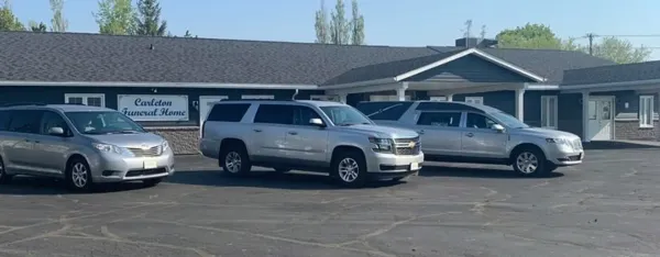 Three silver vehicles parked in front of Carlson Funeral Home on a sunny day.