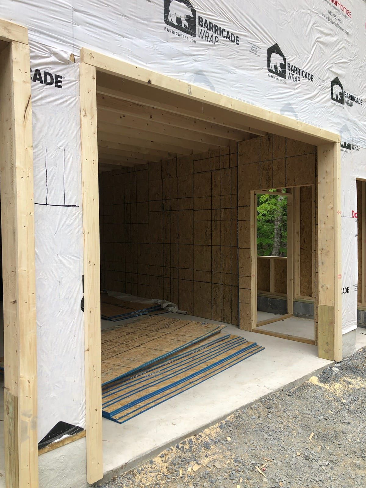 Framed doorway under construction; light wood framing, OSB walls, concrete floor, and Tyvek house wrap.