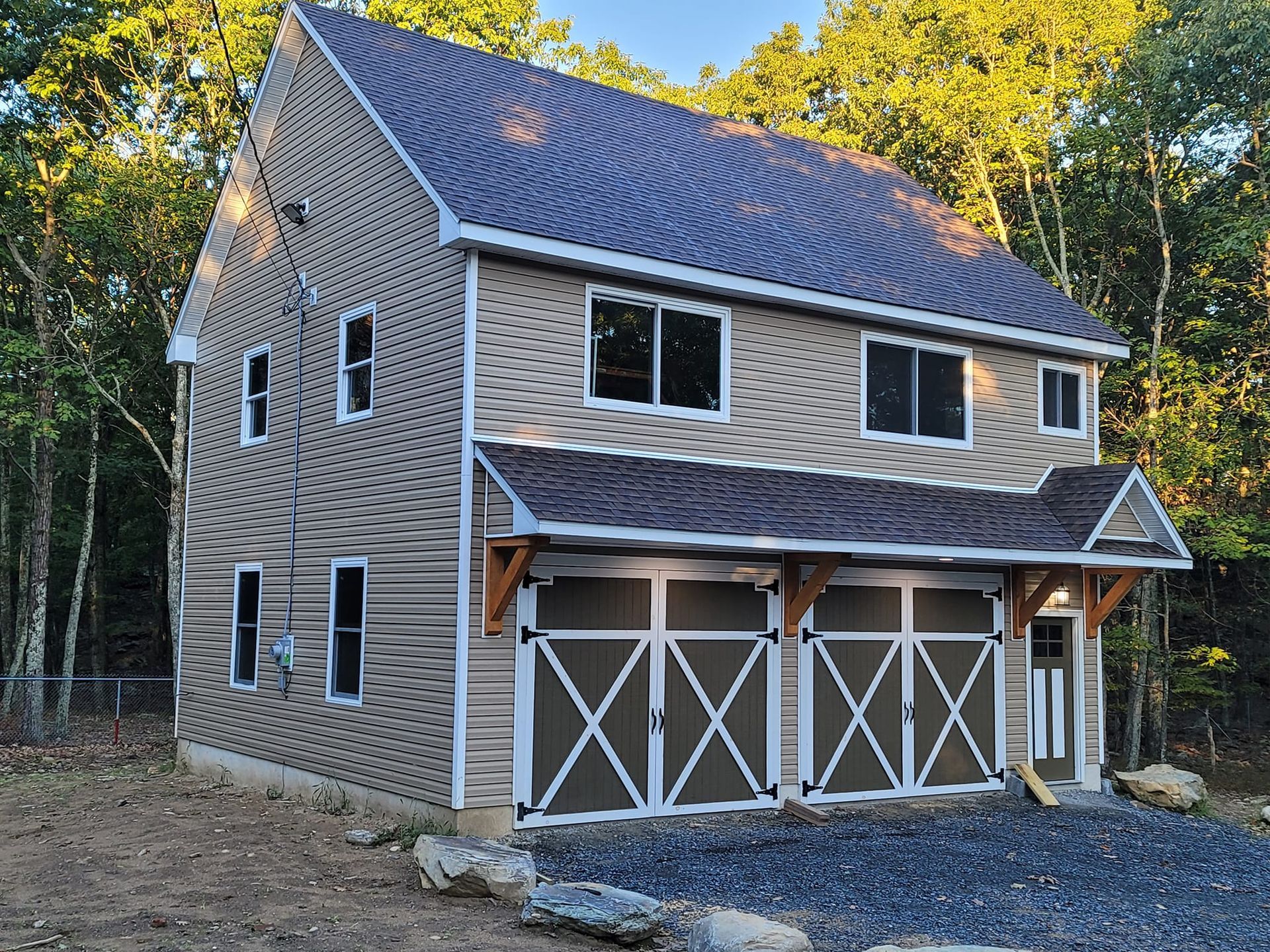Two-story house with brown siding, metal roof, three garage doors, and a wooded backdrop.
