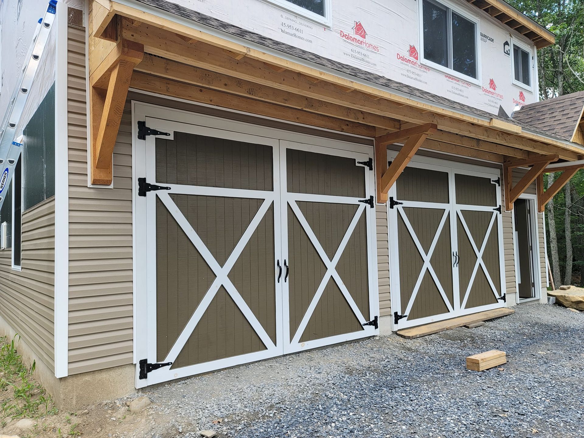 Two-car garage with brown and white barn-style doors, under a wooden overhang, with gray siding.