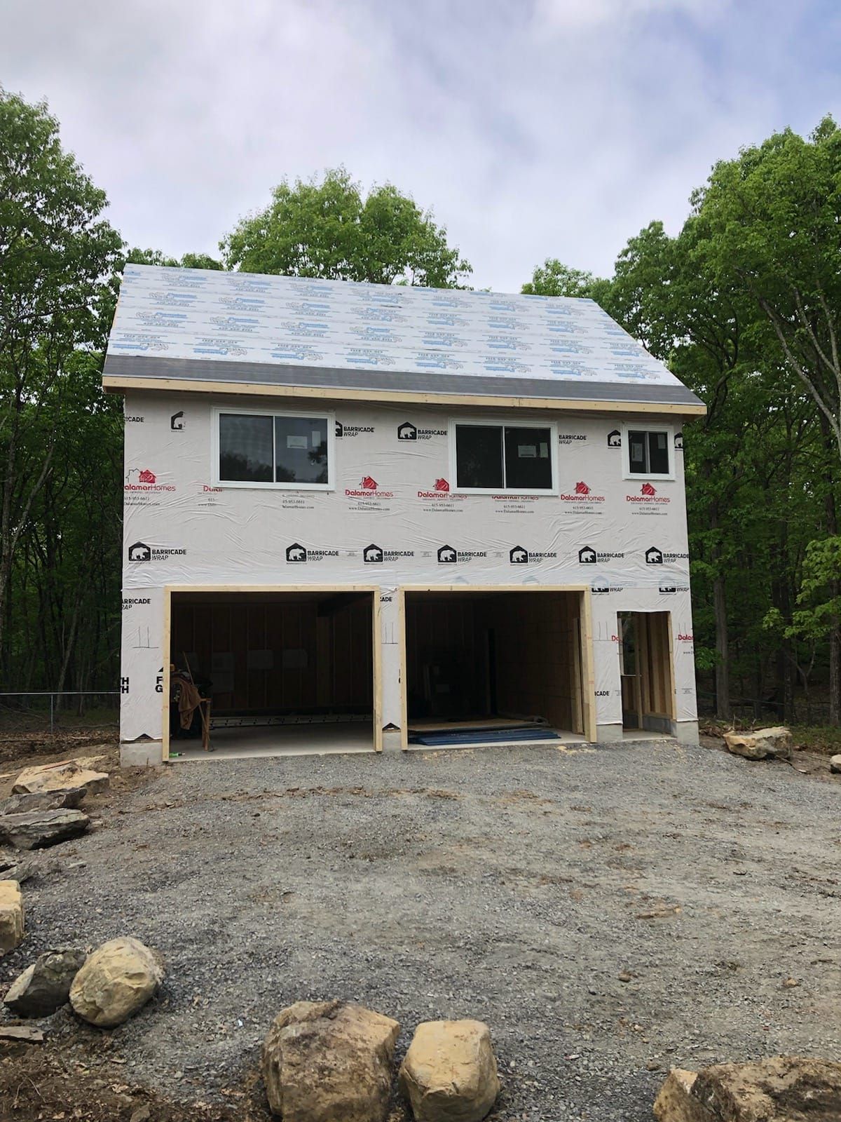 Two-story garage under construction with two bays and windows, set in a wooded area.