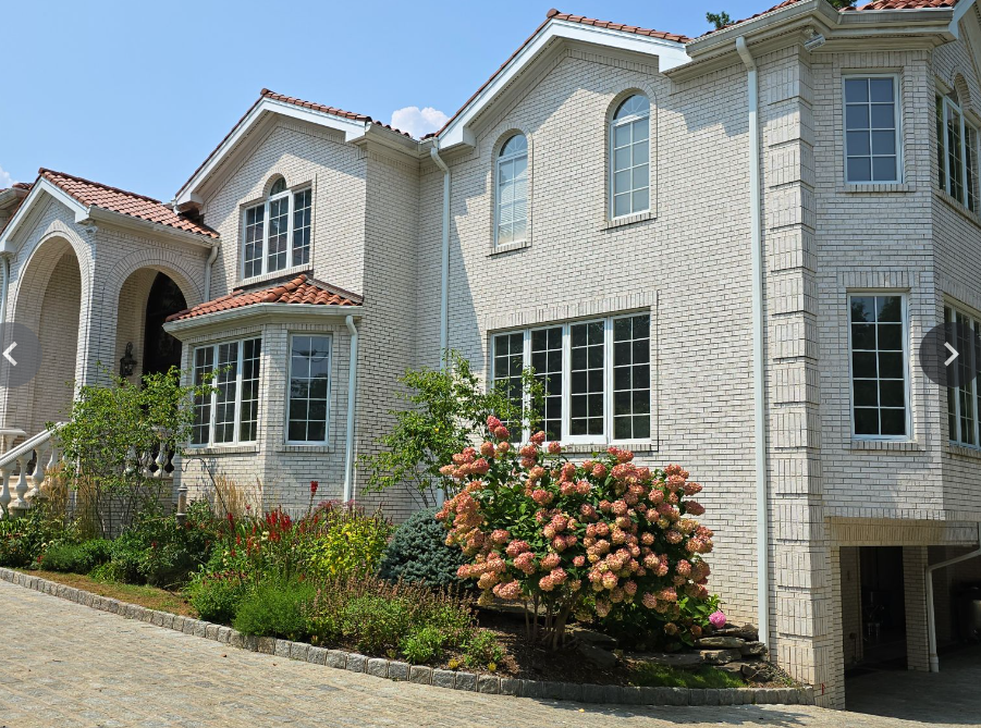 Two-story white brick house with terracotta roof and curved archway over driveway entrance, surrounded by landscaping.