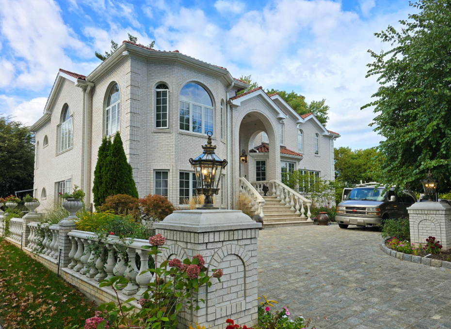 White brick mansion with a stone driveway, arched windows, and a wrought-iron lamp post.