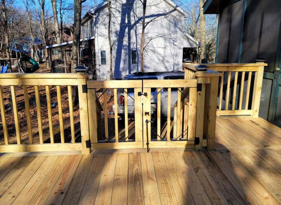 Wooden deck with a gate and railings. Light brown wood, sunny day, residential setting.