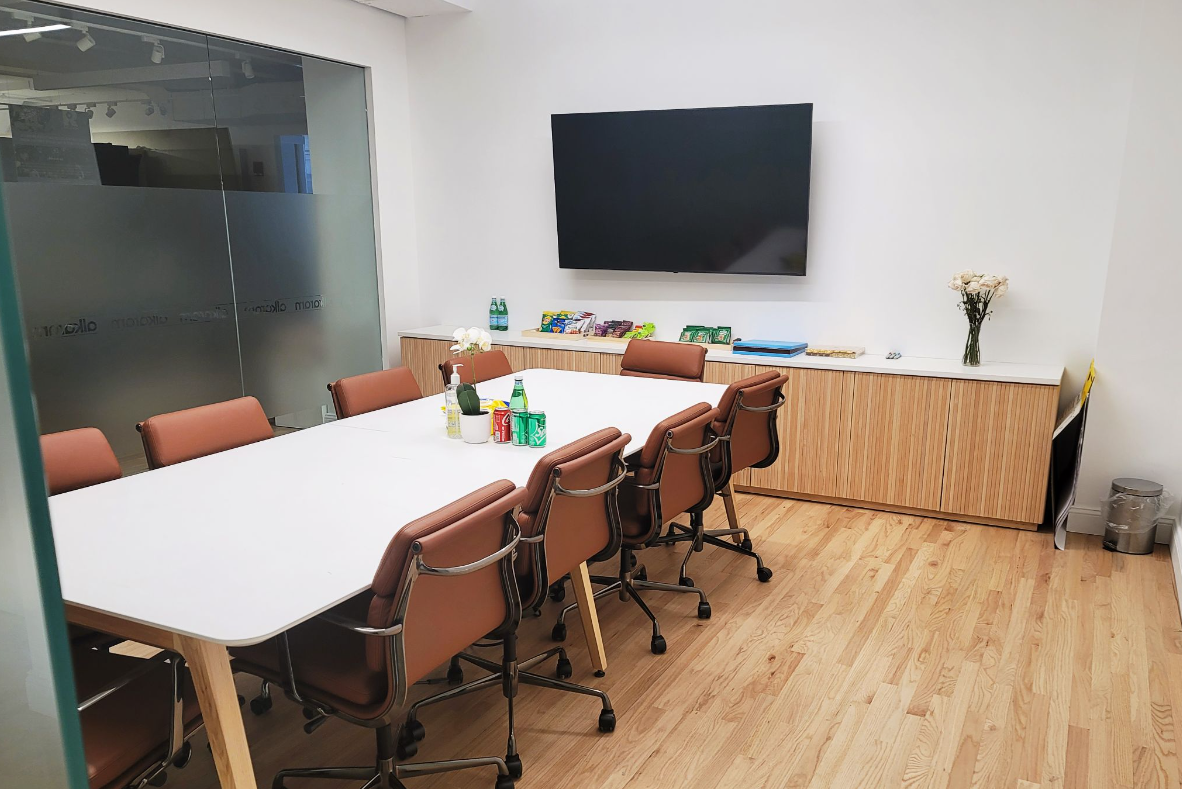 Conference room with long white table, brown chairs, TV, and wood cabinets.