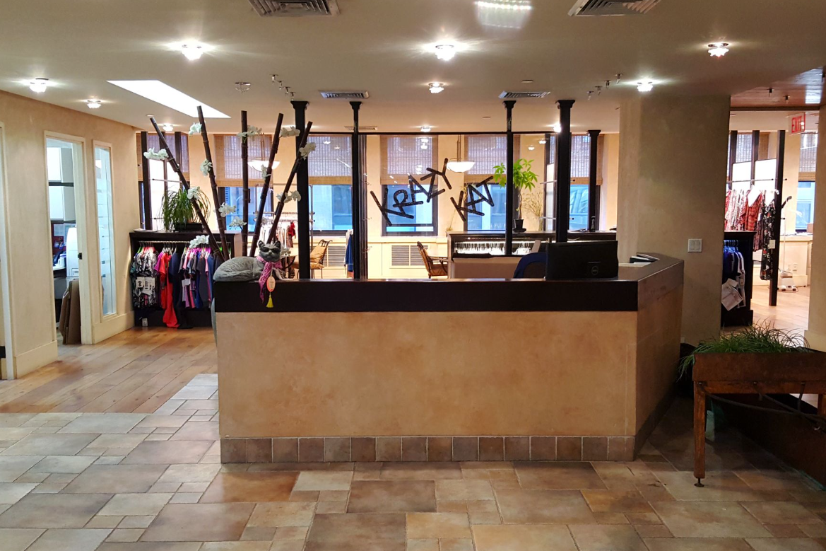 Reception desk with tan stone facade. Black poles hang from the ceiling. Store interior with tile floor.