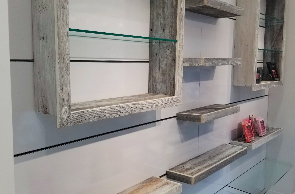 Wooden floating shelves with a rustic finish on a white wall. Some shelves have glass inserts.