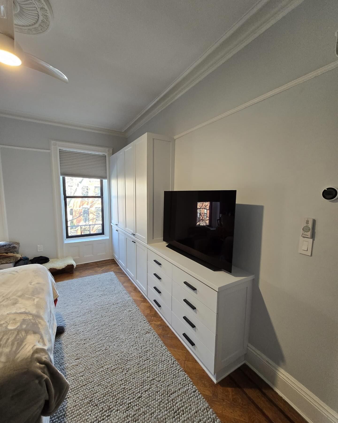 Bedroom with built-in white storage cabinets, a television, and a rug. A window is visible.