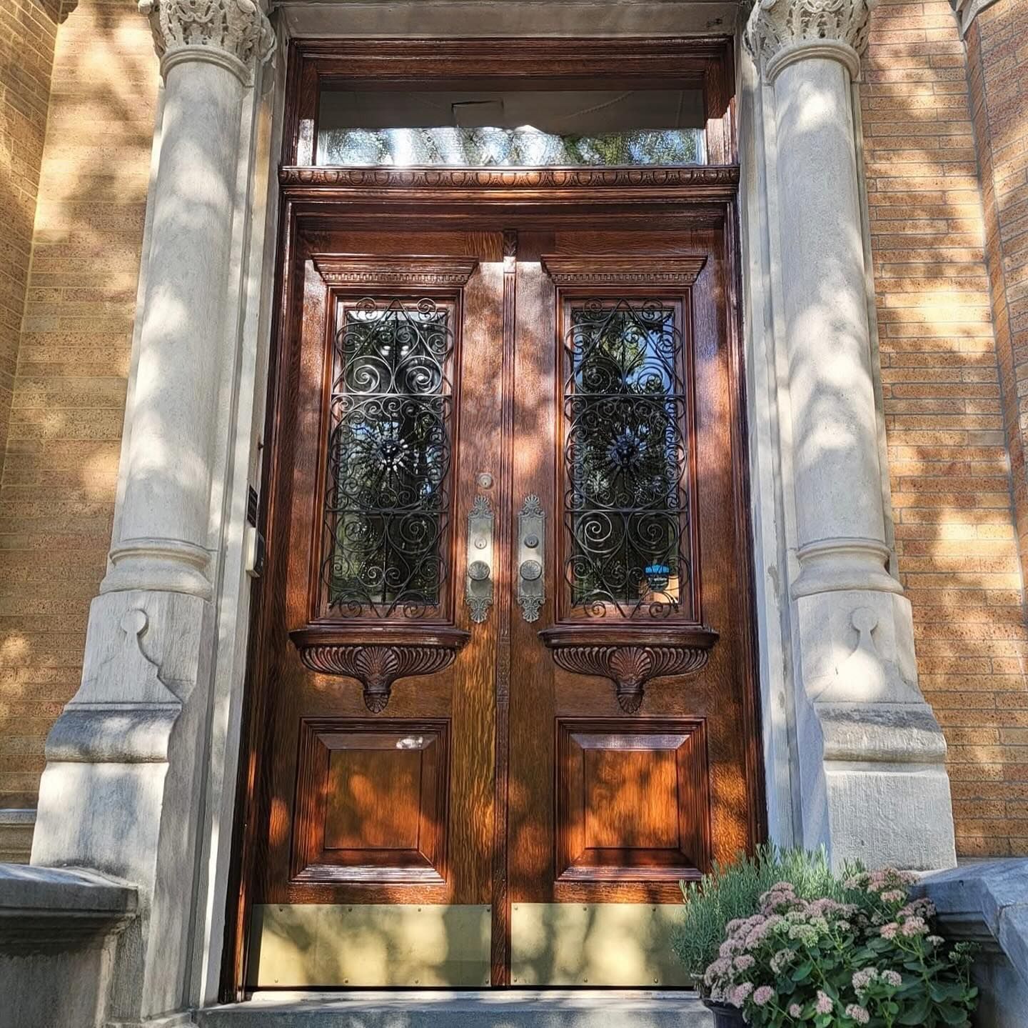 Ornate wooden double doors with stained glass, flanked by stone columns, brick building.