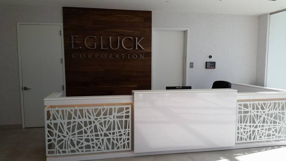 Reception desk with E. GLUCK CORPORATION logo on a dark wood panel, white desk with abstract side panels.