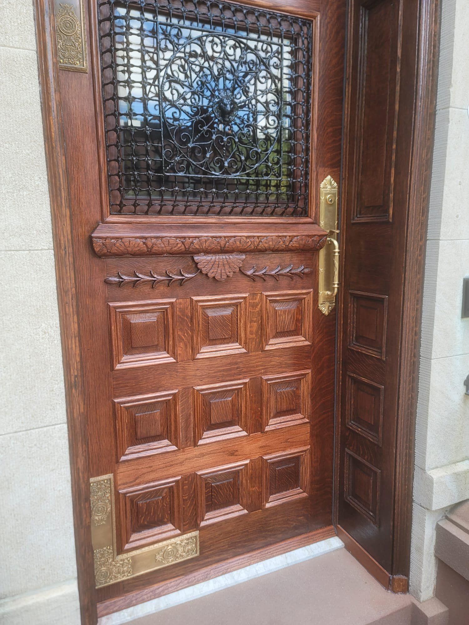 Wooden door with brass hardware and a decorative window, set into a stone wall.