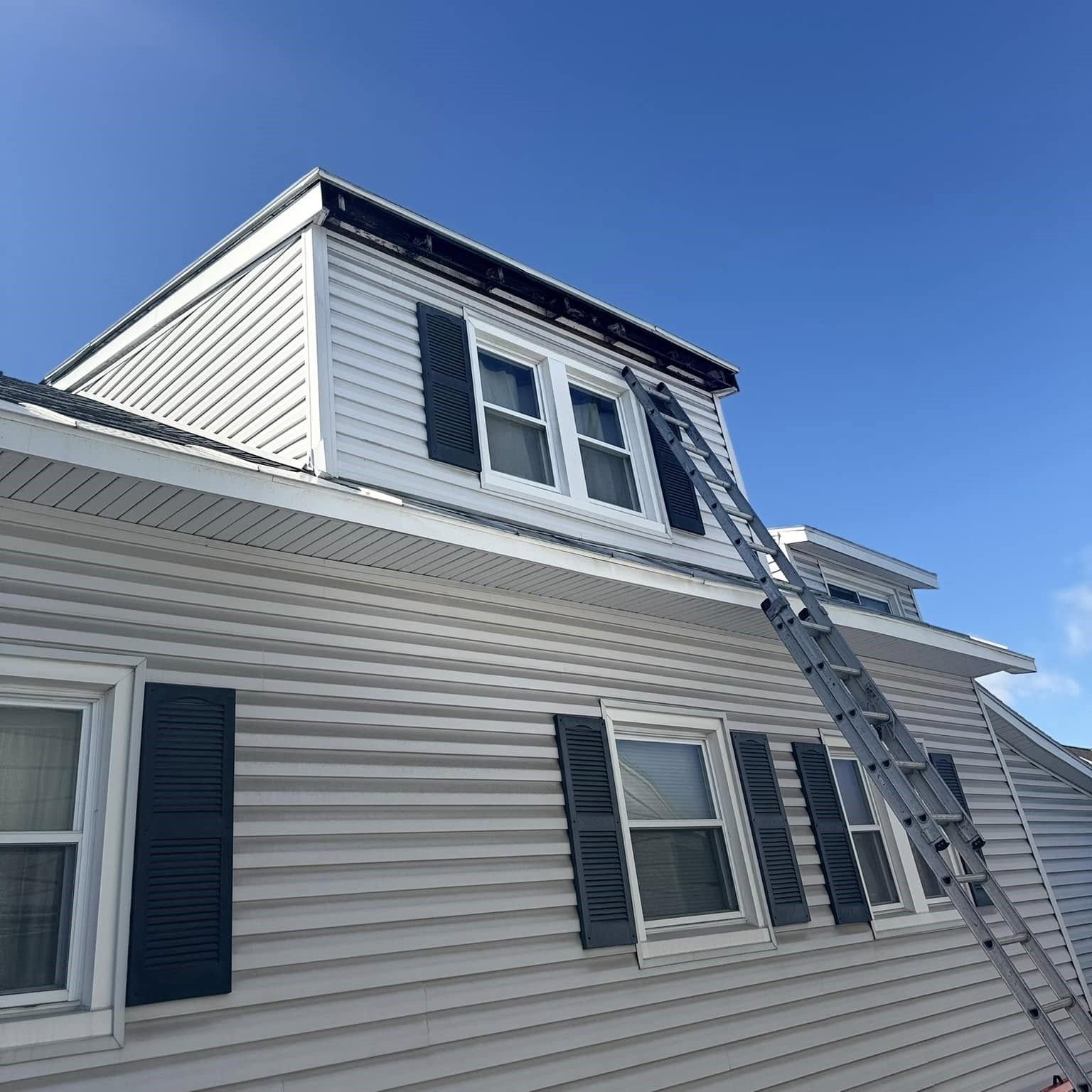 A white house with black shutters and a ladder on the roof. A white house with black shutters and a ladder on the roof.