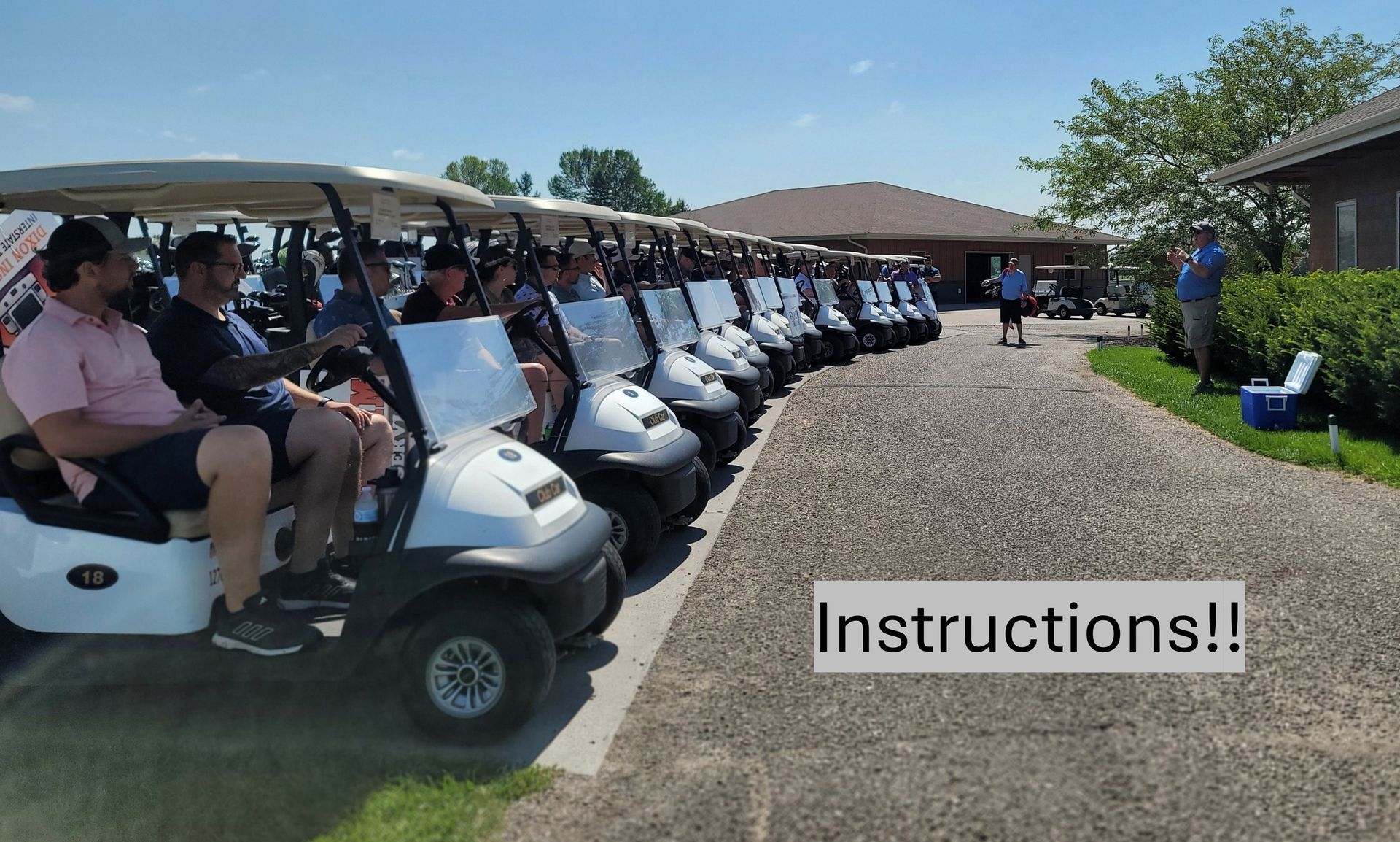Golfers in golf carts lined up, receiving instructions on a sunny day.
