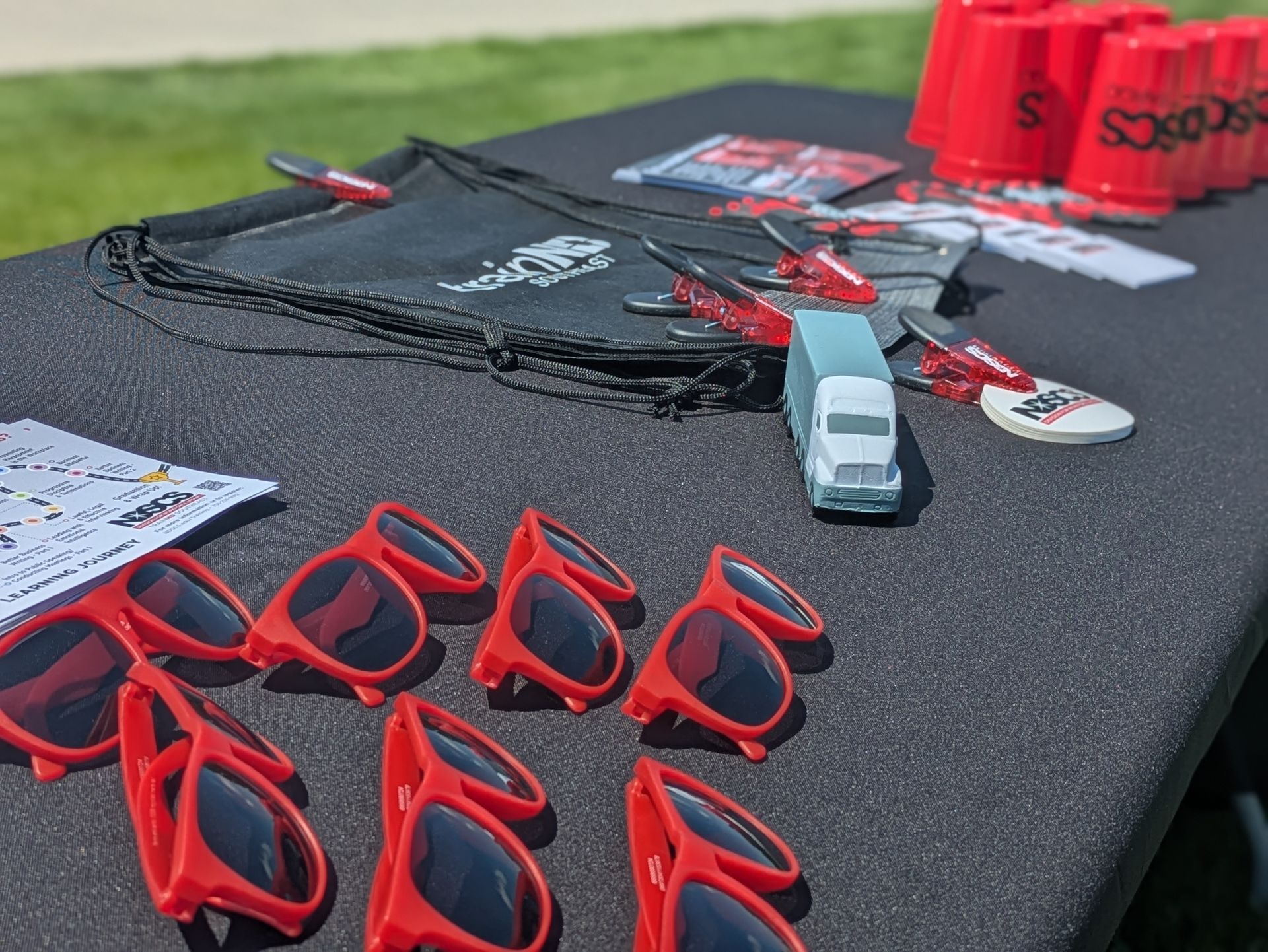 Table with red sunglasses, cups, toys, and swag bags on a sunny day.