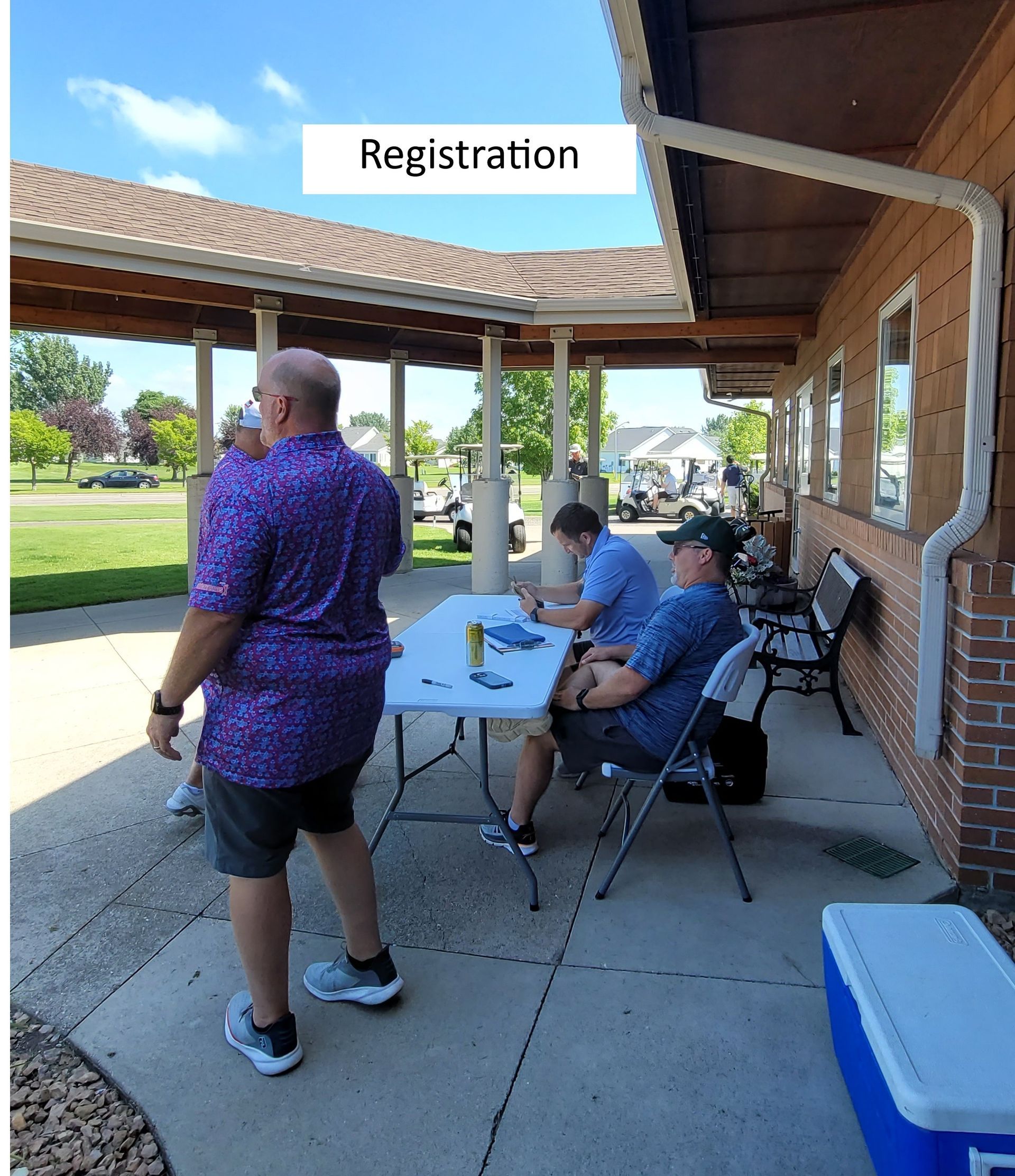 People at a registration table on a covered patio at a golf course.