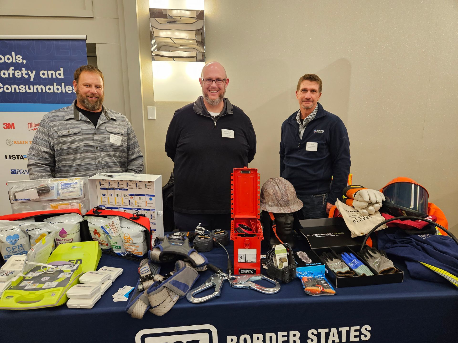 Three men stand behind a table displaying safety equipment.