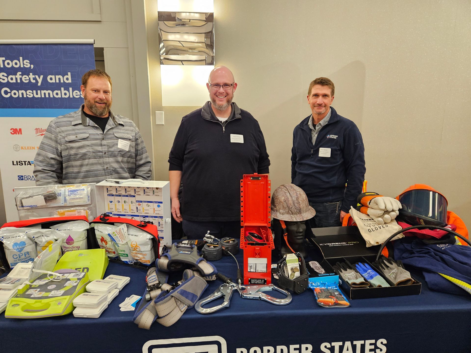 Three men stand behind a table displaying safety tools and supplies.