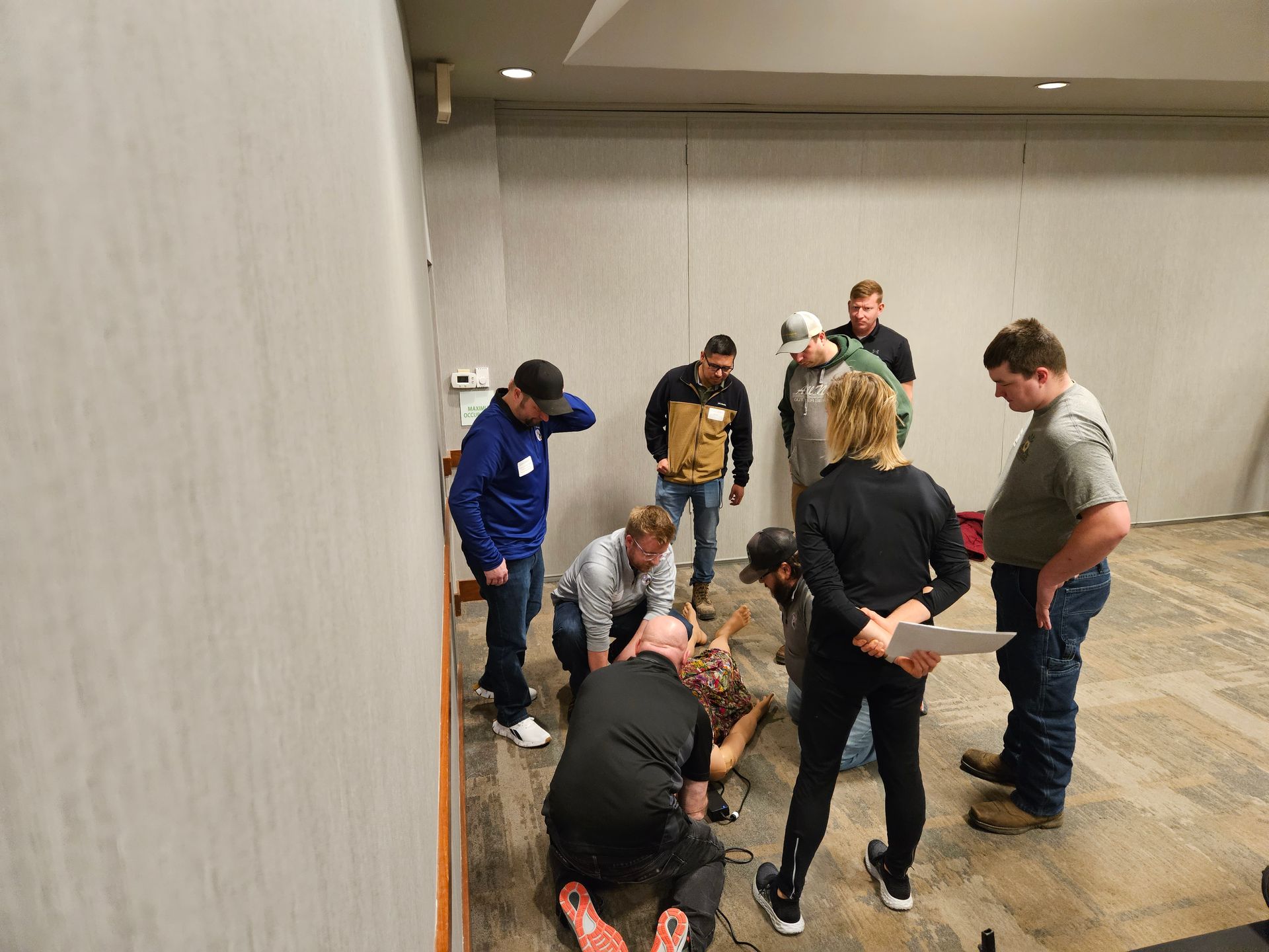 Group of people in a room, some kneeling around a person on the floor. Others look on, assessing the scene.