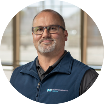 Man with glasses and goatee wearing a blue vest; Marsh & McLennan Agency logo.