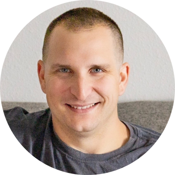 Man with short hair smiles at the camera, wearing a gray shirt, in front of a neutral backdrop.