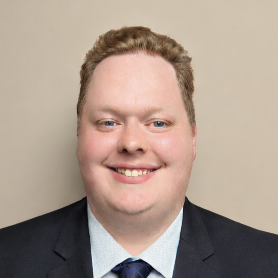Man in suit and tie looking at the camera. He has fair skin and light brown hair.