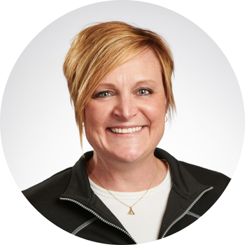 Woman with short blonde hair, smiling, wearing a black zip-up jacket over a white shirt.