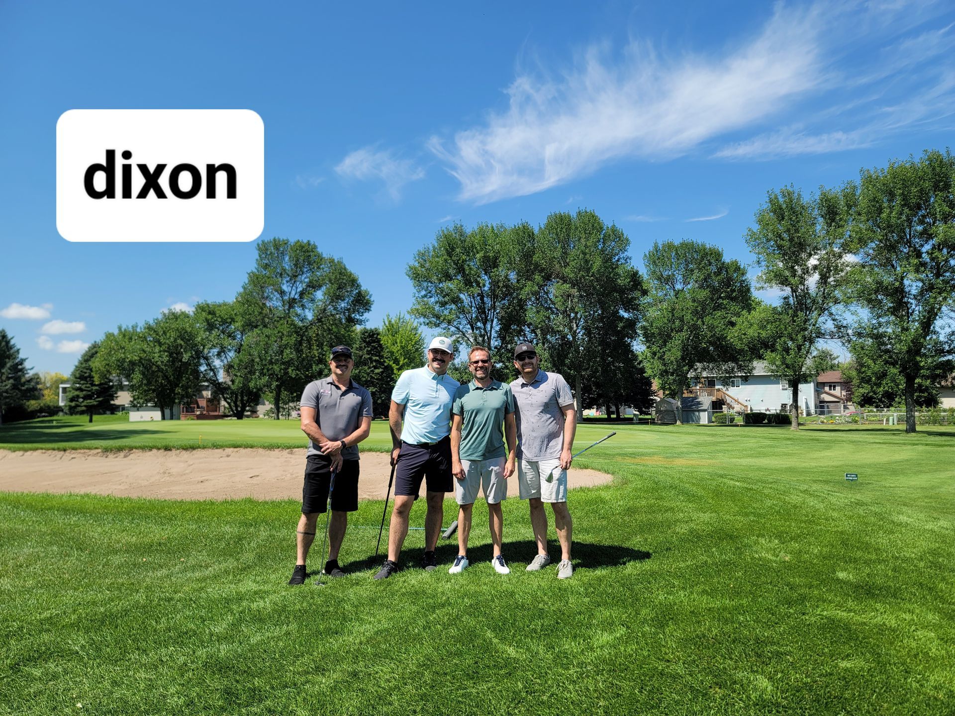 Four people standing on a golf course under a blue sky, with the word 