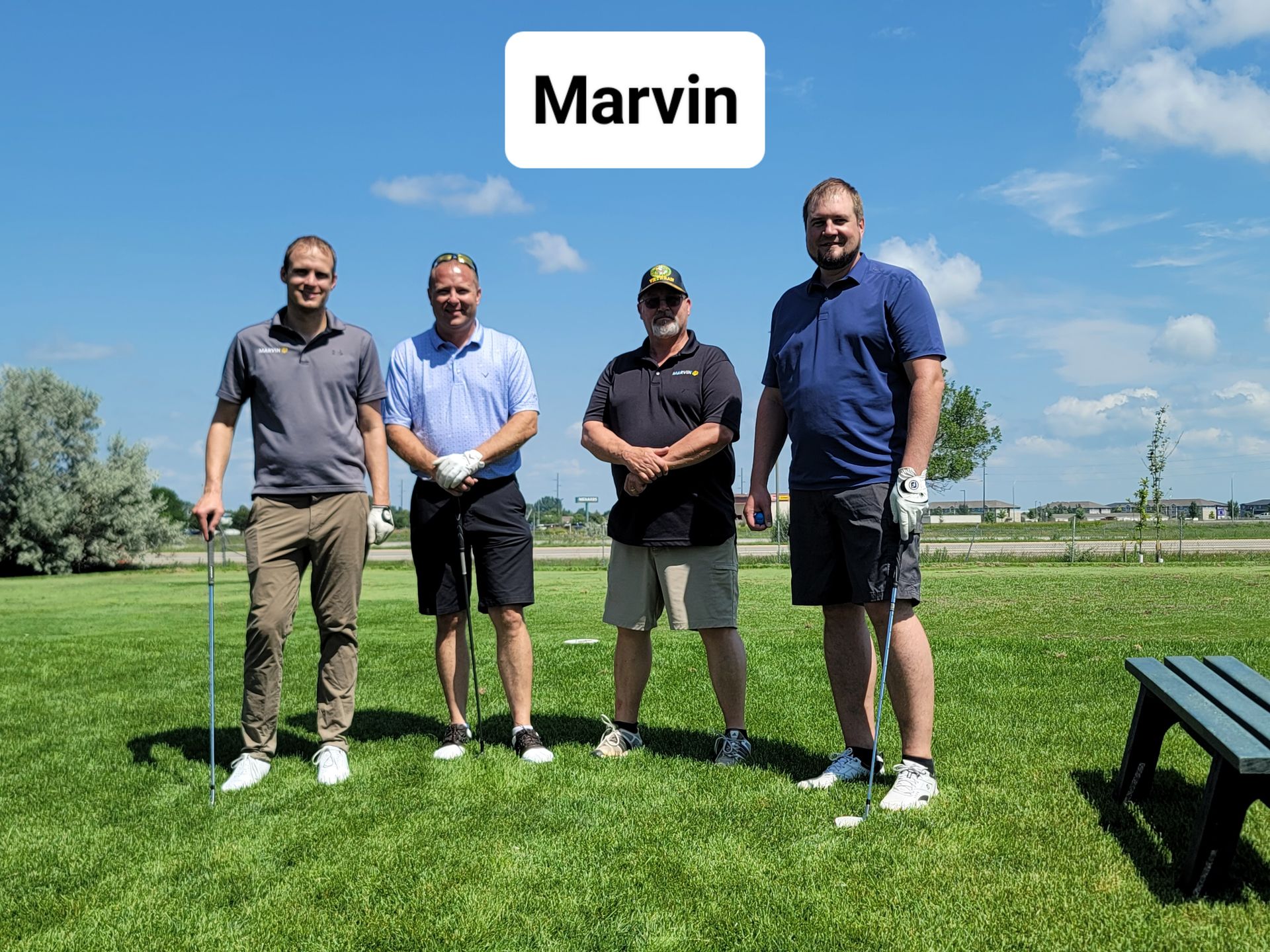 Four men on a green golf course, with golf clubs. A white box reads 