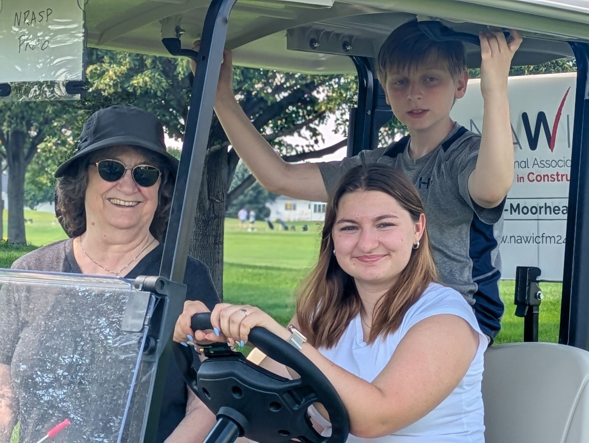 Three people smiling in a golf cart on a green course; woman driving, boy & woman in the back.