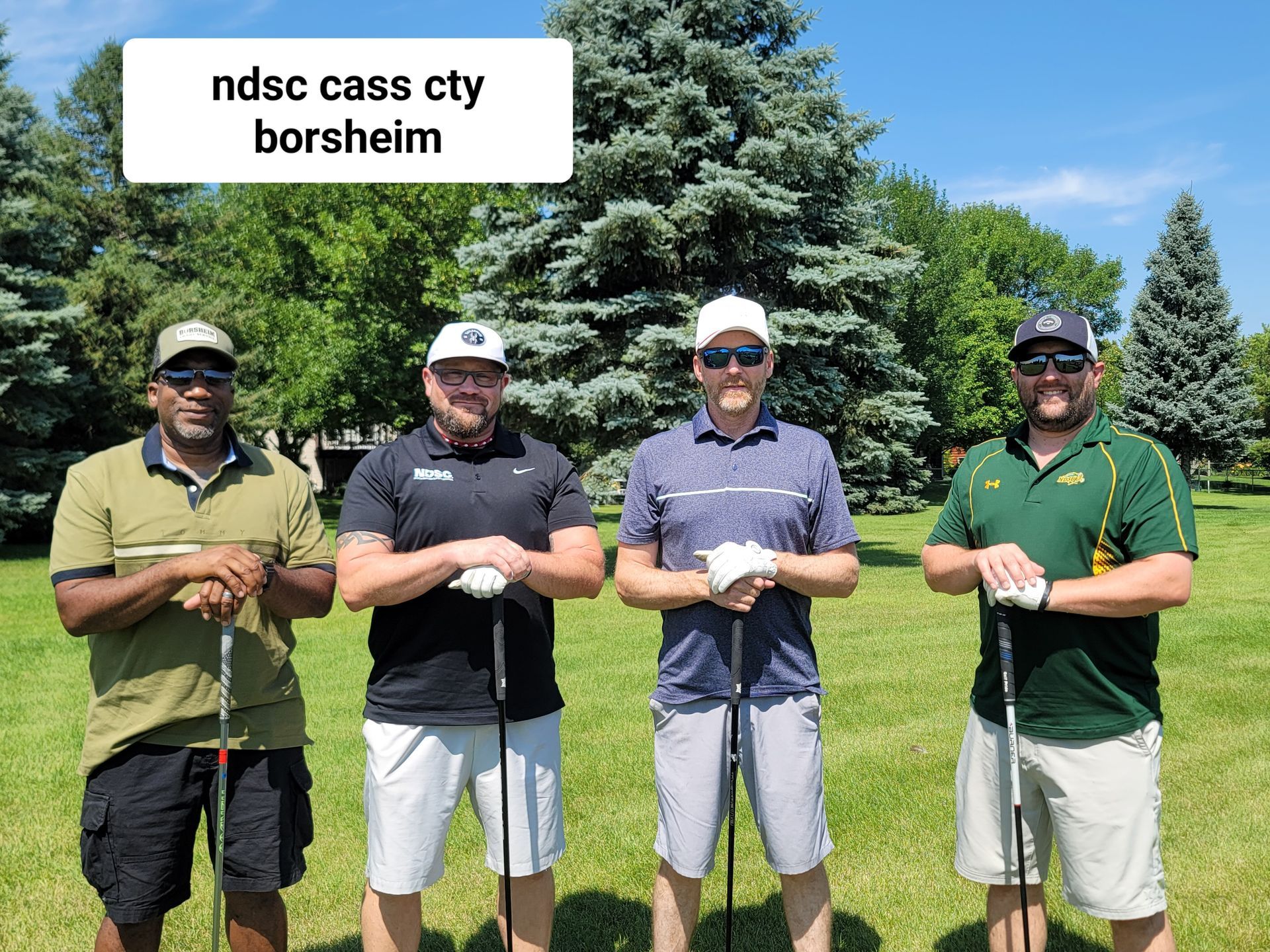 Four men with golf clubs on a green lawn, standing near trees; text reads 