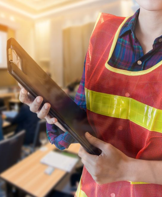 Person wearing a reflective vest holding a clipboard in a classroom setting.