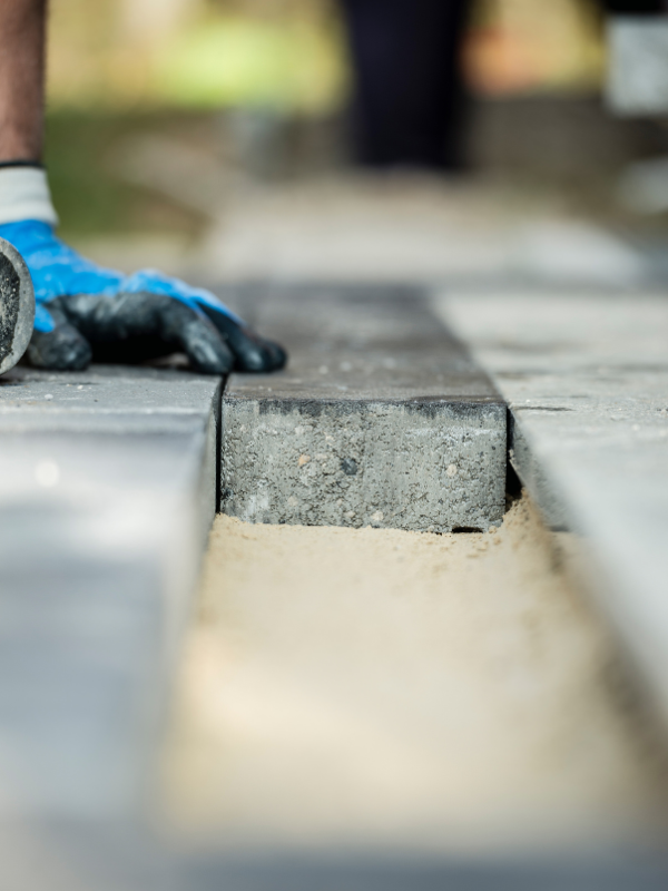 A person wearing blue gloves is laying bricks on a sidewalk.