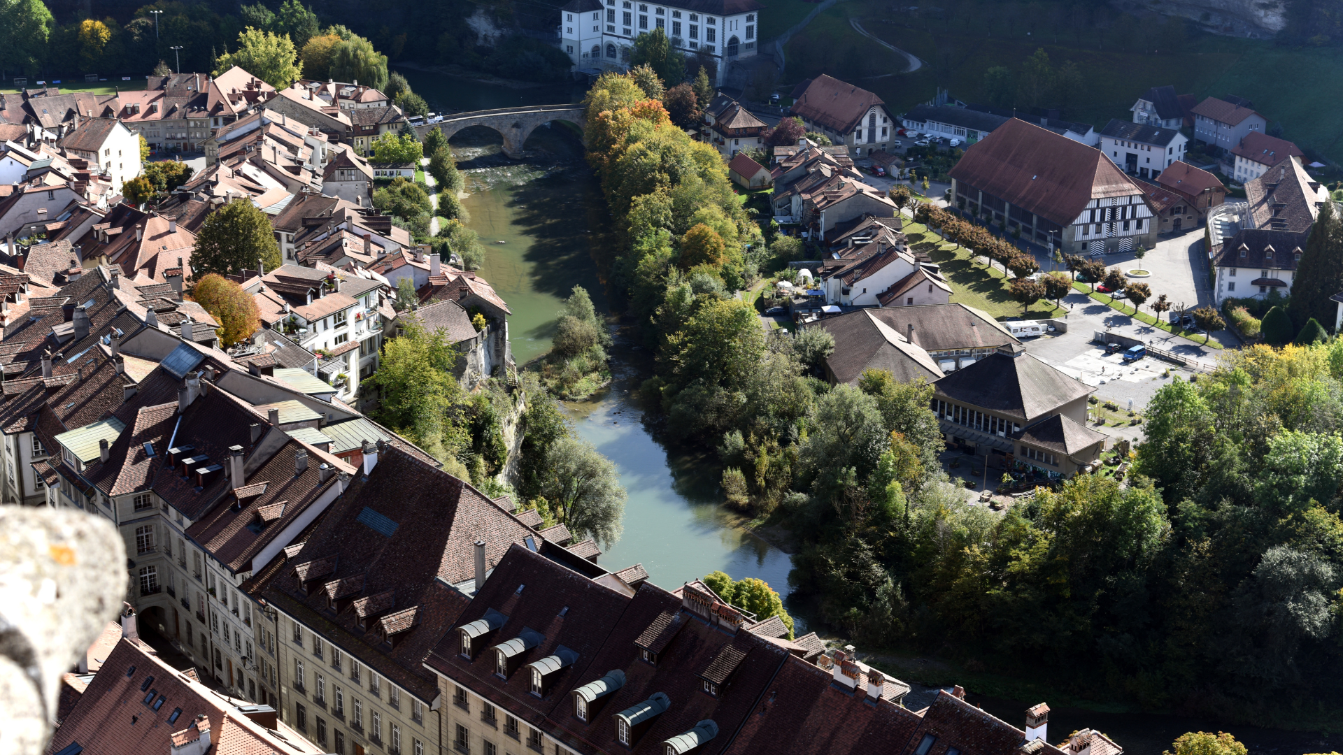 Aerial view of a European town with a river, bridge, buildings with brown roofs, and trees.