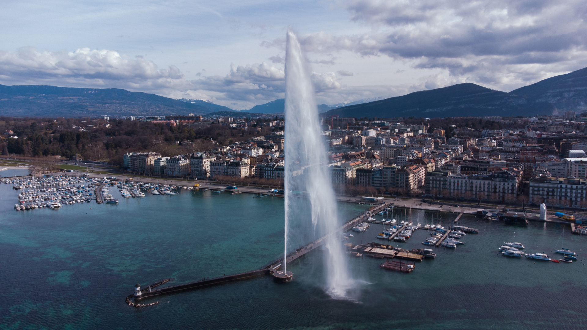 Jet d'Eau fountain spraying water high over Geneva, Switzerland. Boats and city buildings visible.