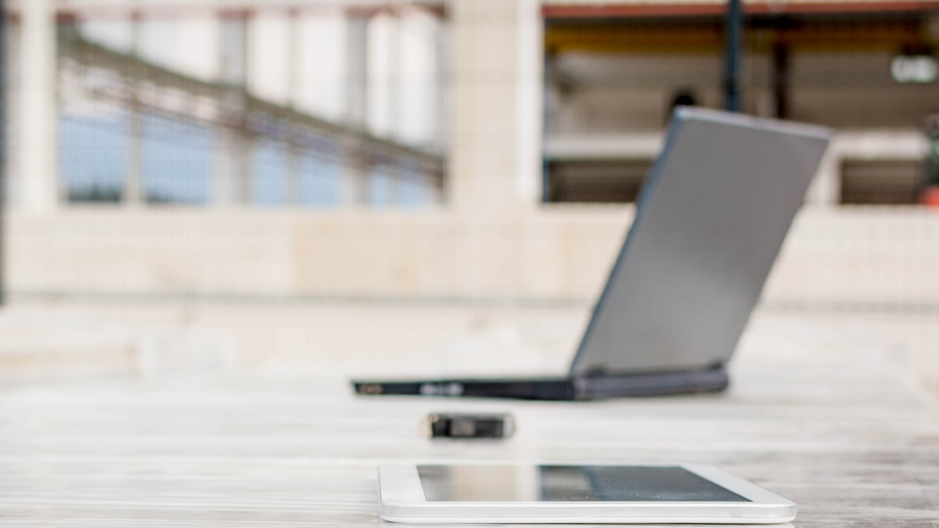Laptop and tablet on a light-colored surface with a blurred building in the background.