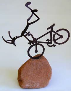 Metal sculpture of a cyclist on a bicycle, balancing on a rock.