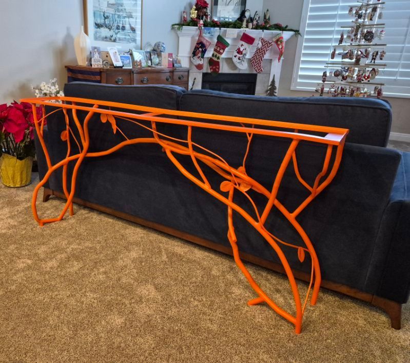 Orange metal console table shaped like branches against a dark blue sofa in a living room.