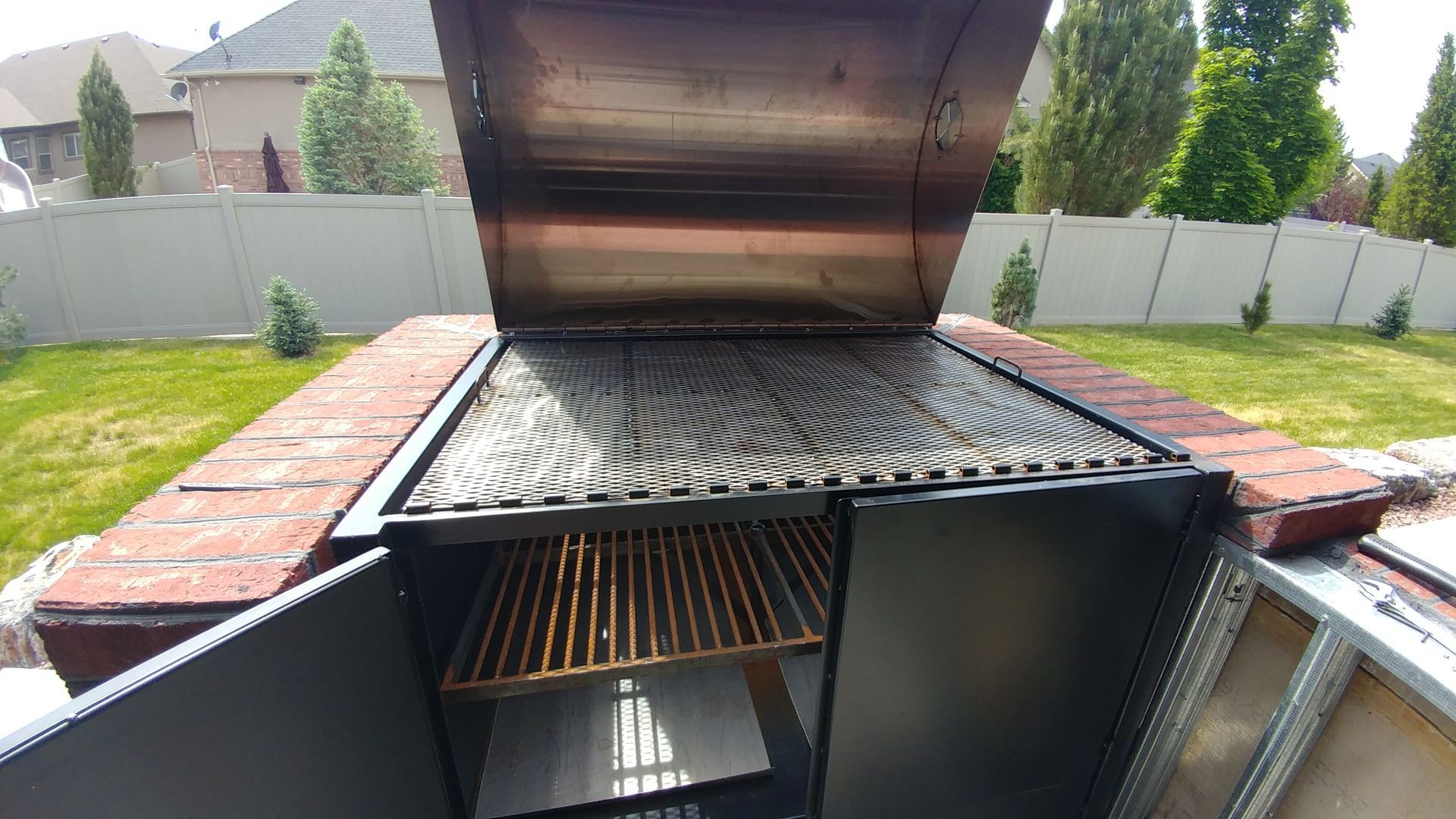 Outdoor brick barbecue grill with open lid, metal grates, and storage below.
