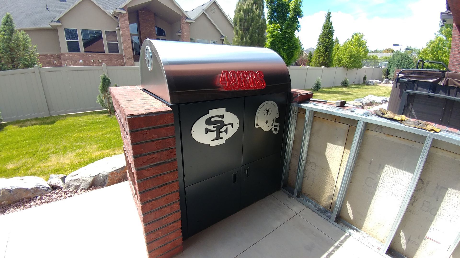 Black barbecue grill with brick supports, custom logo, copper finish, and patio setting.