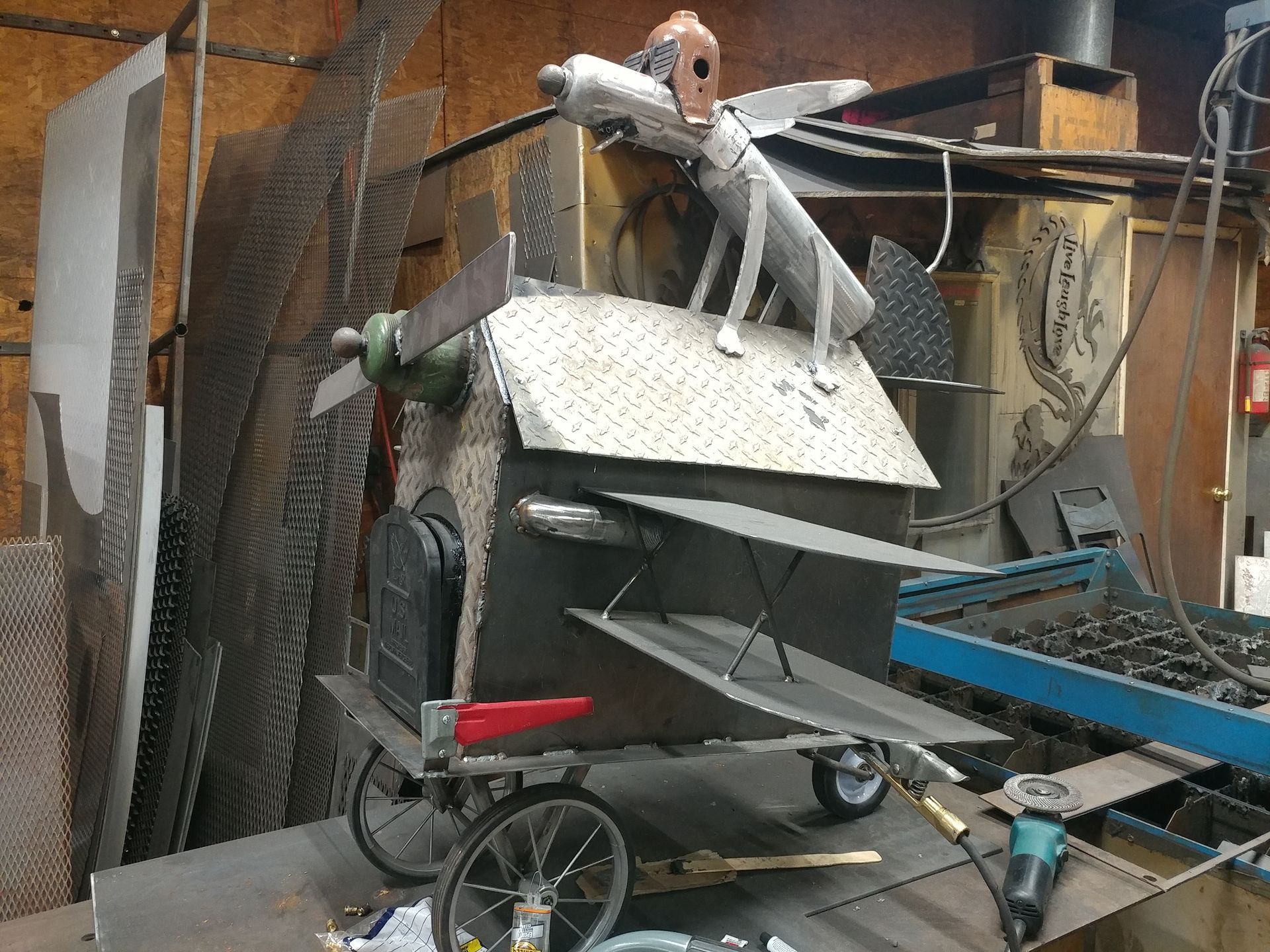 Metal sculpture of an airplane-themed mailbox with propeller, wings, and a dog pilot figure.