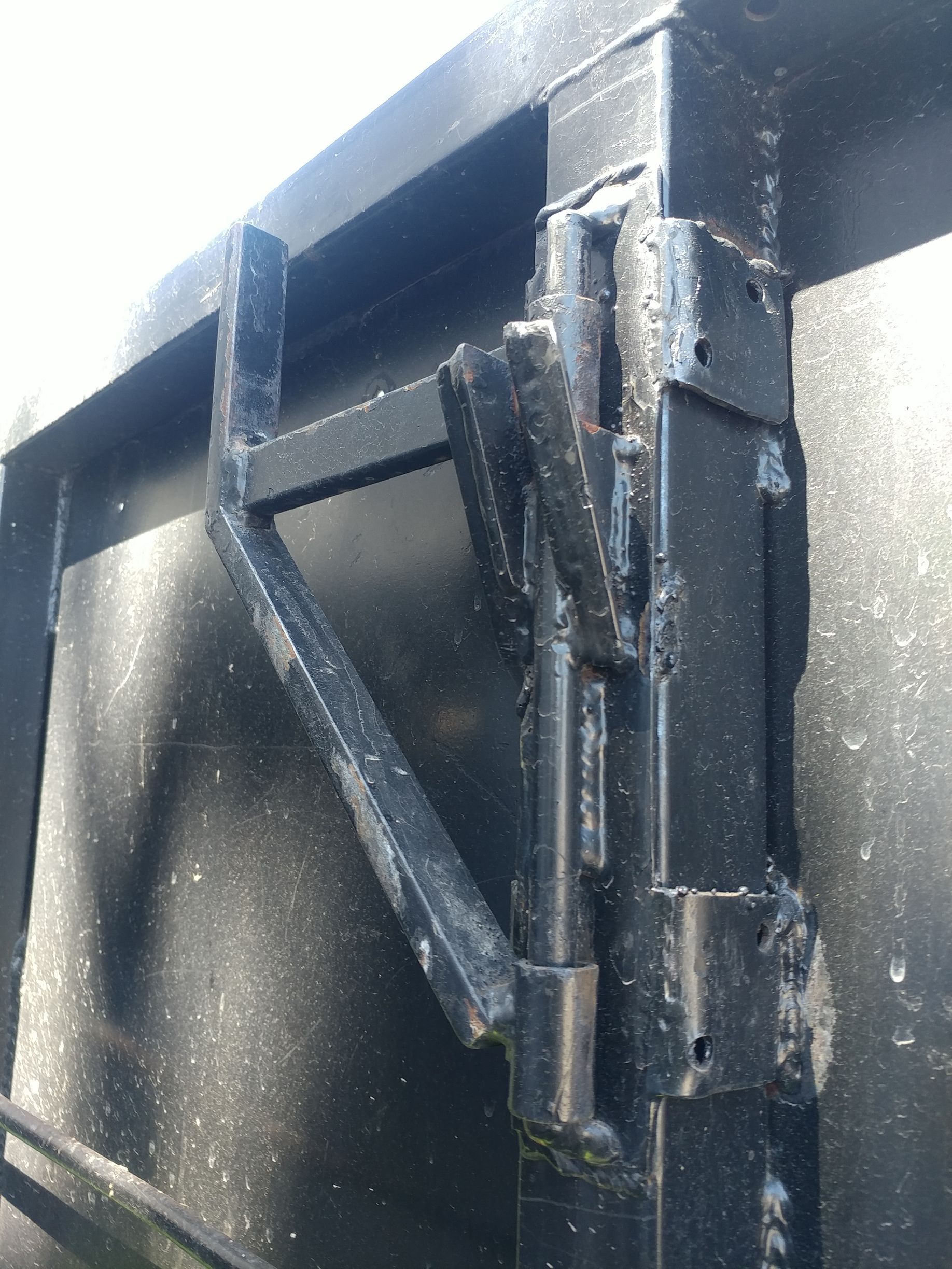 Black metal latch on a dark surface, possibly a gate or door, outdoors.